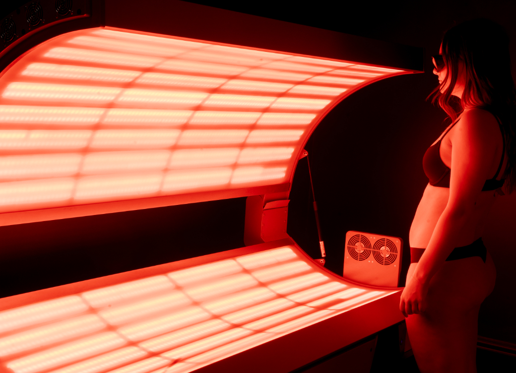 A woman stands in front of a tanning bed, preparing for a red light therapy session.