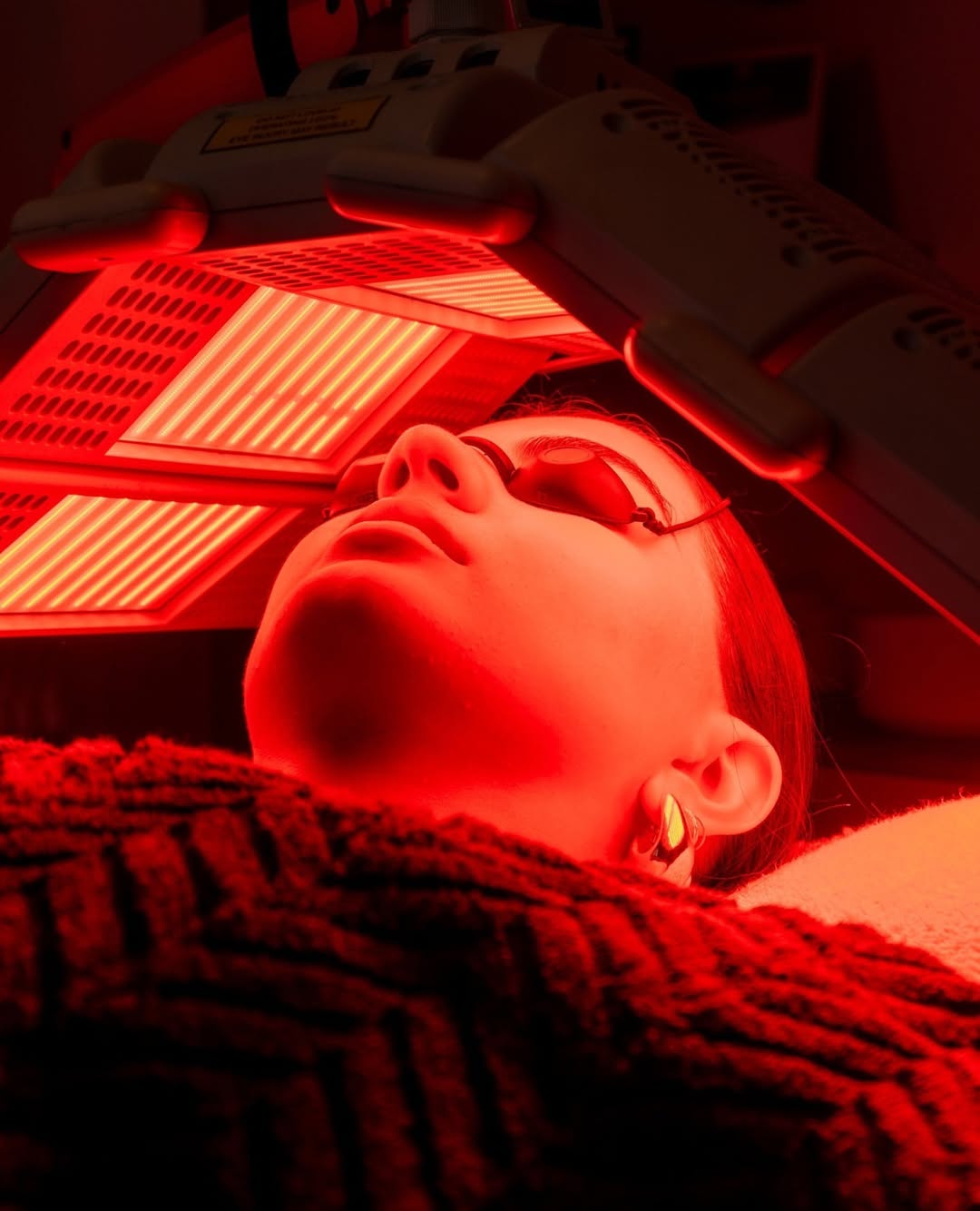 A woman rests in a chair, her face bathed in a warm red light, suggesting a calming or therapeutic environment.