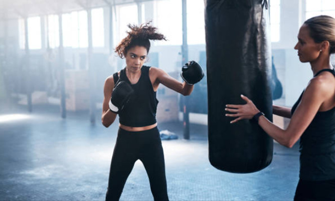 Inside a boxing gym, two women focus on a punching bag, showcasing their training routine.